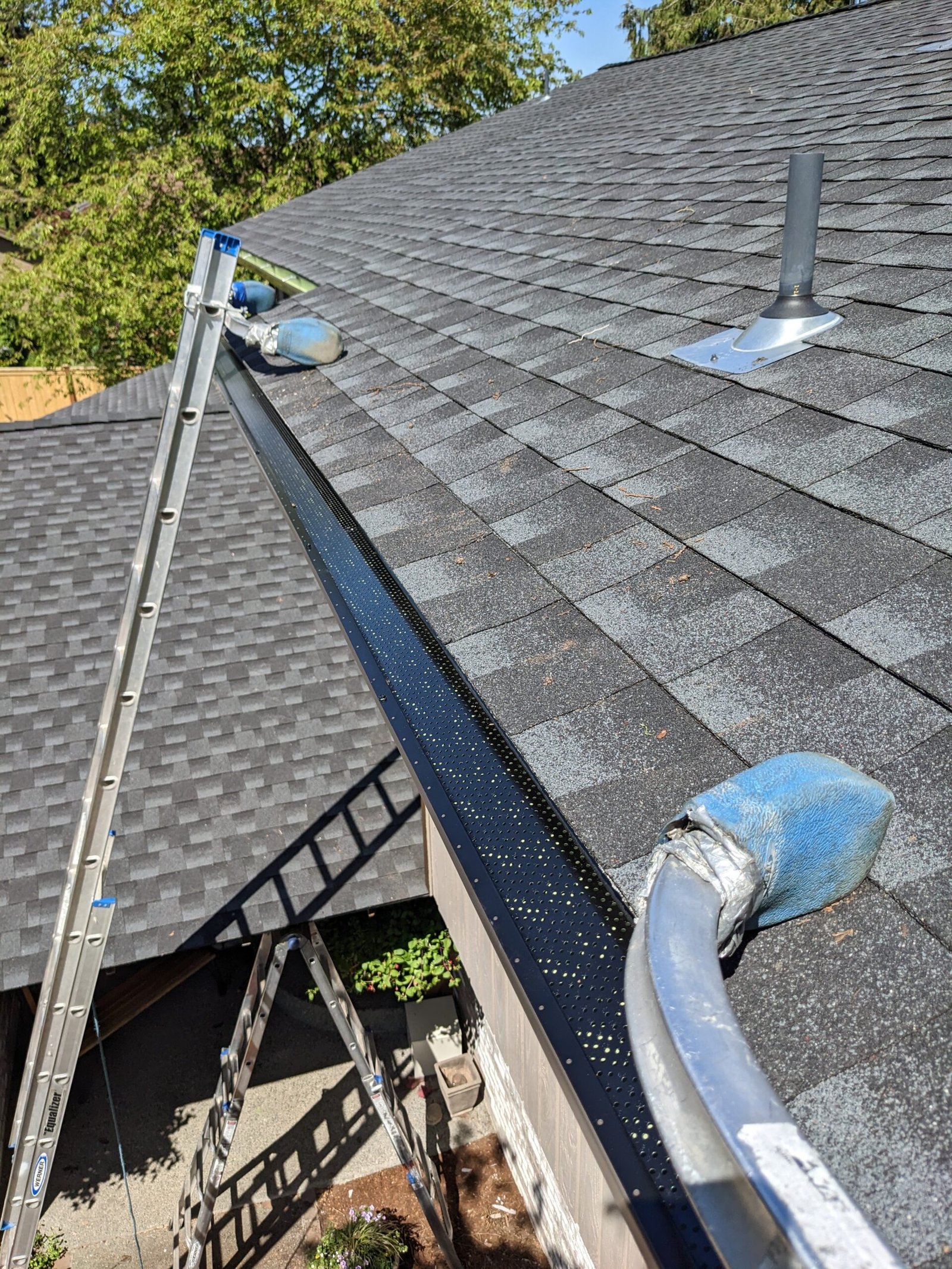 Perforated gutter guard along a shingle roof edge